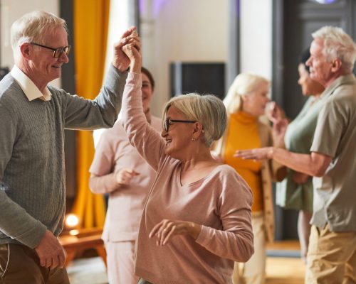 Group of smiling senior people dancing while enjoying activities in retirement home, copy space